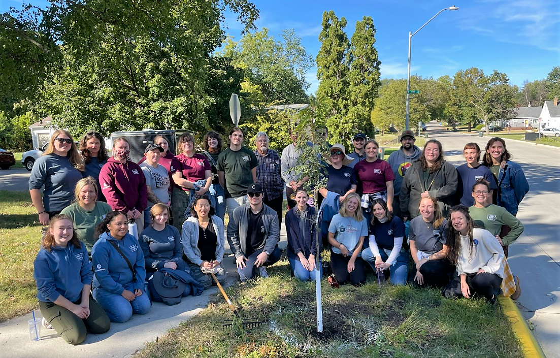 Large group of people posing around a newly planted tree